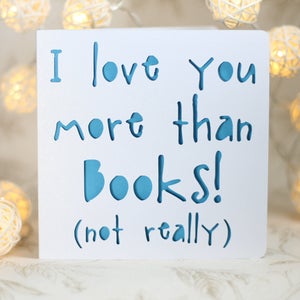 May include: White card with blue text that reads "I love you more than books! (not really)"