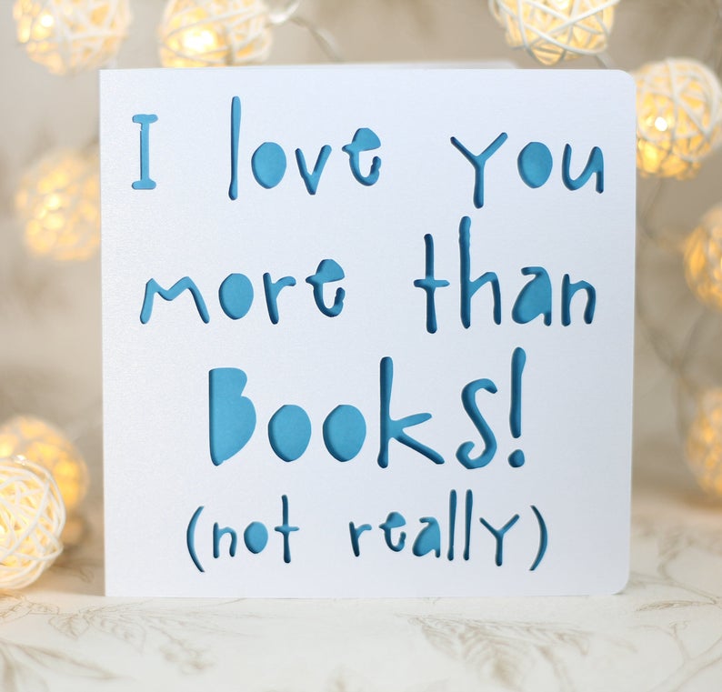 May include: White card with blue text that reads "I love you more than books! (not really)"