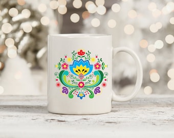 Könnte beinhalten: Weiße Keramiktasse mit einem bunten Blumendesign mit blauen, gelben, roten, grünen und pinkfarbenen Blumen. Das Design erinnert an traditionelle Volkskunst.