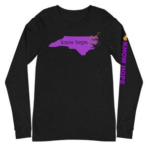 Peut inclure: T-shirt noir &agrave; manches longues avec un contour violet de la Caroline du Nord et les mots "know hope". La manche droite porte l'inscription "KNOW HOPE" en violet. Des papillons dor&eacute;s sont pr&egrave;s de la c&ocirc;te.