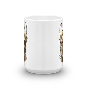 May include: White ceramic mug with a brown and white cat illustration on both sides. The cat is wearing a hat and has a surprised expression.