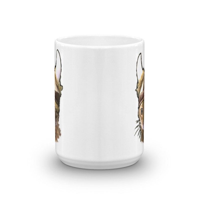 May include: White ceramic mug with a brown and white cat illustration on both sides. The cat is wearing a hat and has a surprised expression.