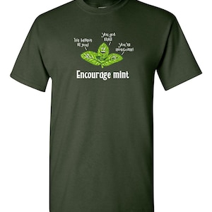 An olive green t-shirt printed with a graphic of smiling mint leaves and the text Encourage mint.