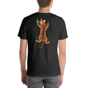 Pode incluir: Uma camiseta preta com um gr&aacute;fico de um gato com estampa de leopardo pendurado de cabe&ccedil;a para baixo com as garras estendidas.