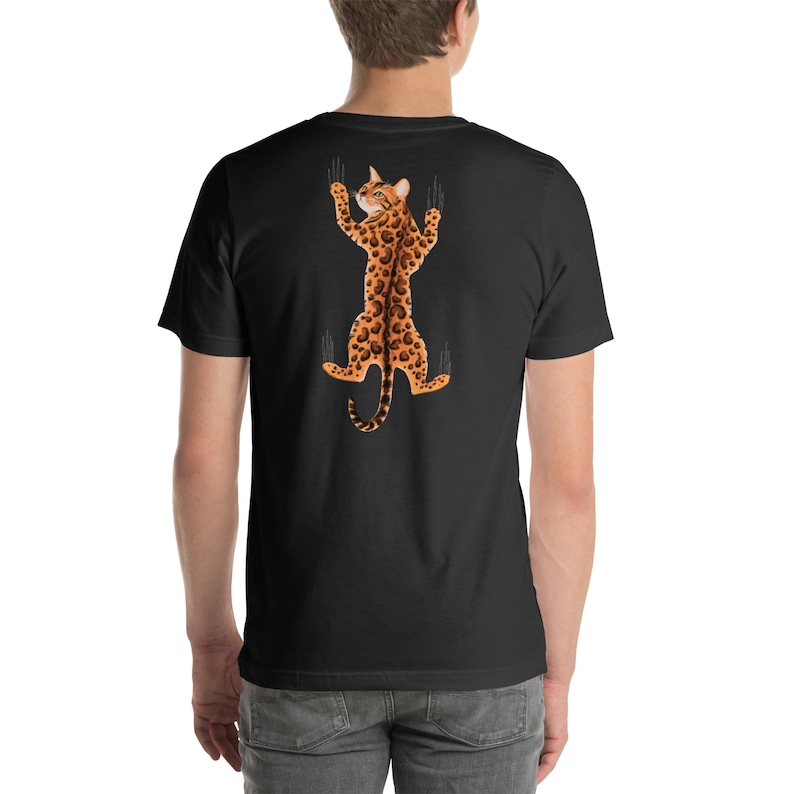 Pode incluir: Uma camiseta preta com um gr&aacute;fico de um gato com estampa de leopardo pendurado de cabe&ccedil;a para baixo com as garras estendidas.