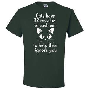 May include: A dark green t-shirt with a white graphic of a cat's face and the text "Cats have 32 muscles in each ear to help them ignore you."