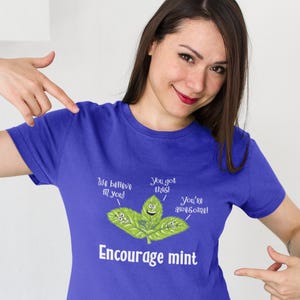 A woman points to a blue t-shirt printed with smiling mint leaves and the text Encourage mint.