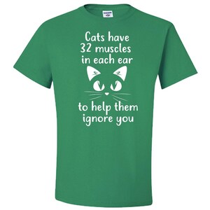 May include: Green t-shirt with a white cat face and the text "Cats have 32 muscles in each ear to help them ignore you."