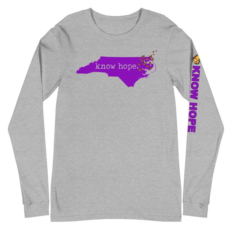 Peut inclure: Un t-shirt gris &agrave; manches longues avec un contour violet de la Caroline du Nord et les mots "know hope". La manche droite affiche "KNOW HOPE" en violet et un motif de papillon.