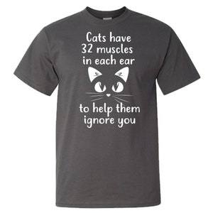 May include: Dark gray t-shirt with a white cat face and the text "Cats have 32 muscles in each ear to help them ignore you."