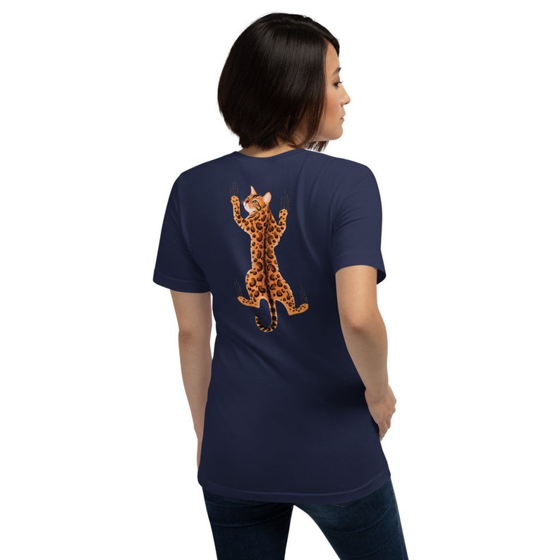 Pode incluir: Uma camiseta azul marinho com um gr&aacute;fico de um gato com estampa de leopardo agarrado &agrave; parte de tr&aacute;s da camiseta.
