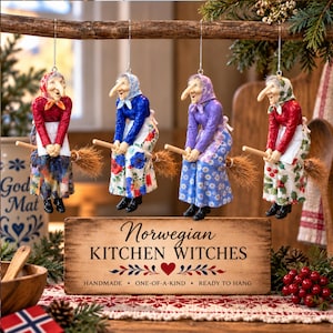 May include: Four hanging ornaments of witches riding broomsticks, each wearing a headscarf, long-sleeved top, and patterned apron. A wooden sign below reads: Norwegian KITCHEN WITCHES, HANDMADE, ONE-OF-A-KIND, READY TO HANG, with a red heart icon.