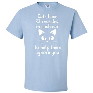 May include: Light blue t-shirt with a white cat face and the text "Cats have 32 muscles in each ear to help them ignore you."