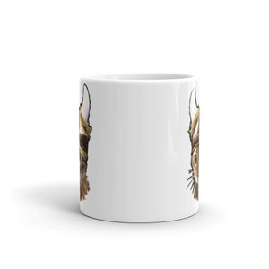 May include: White ceramic mug with a brown and white cat wearing a viking helmet printed on both sides.