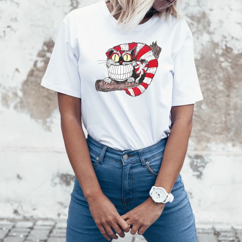 May include: White t-shirt with a graphic of a red and white striped cat with a large grin and yellow eyes. The cat is sitting on a branch.