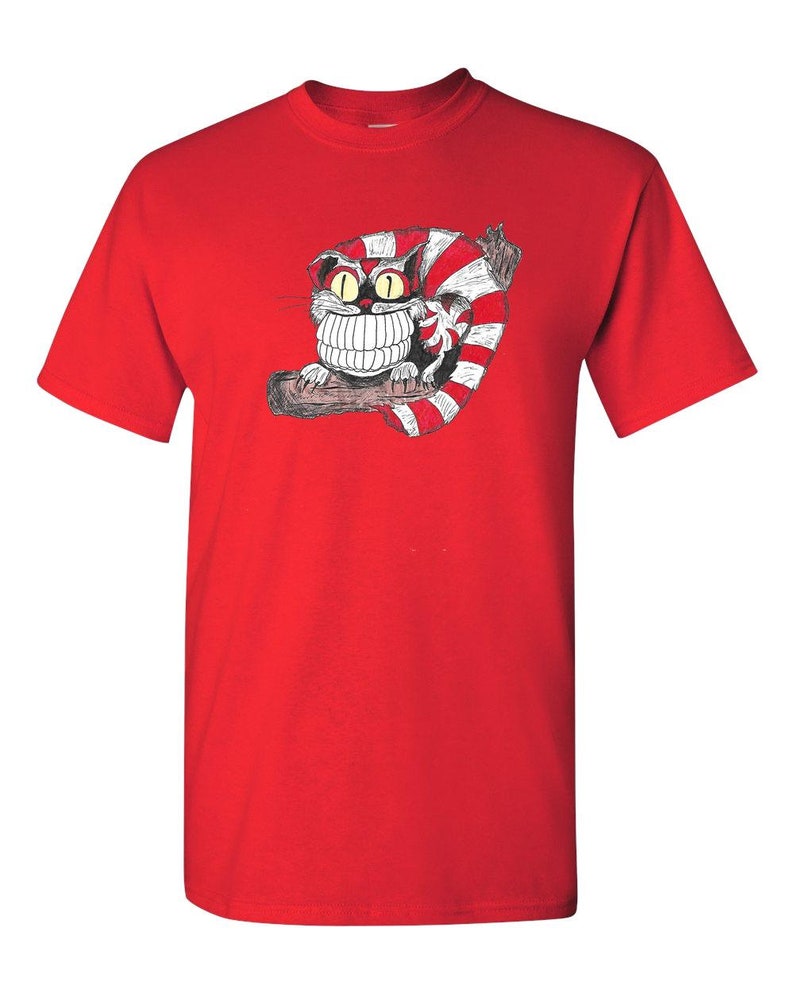 May include: Red t-shirt with a cartoon Cheshire Cat from Alice in Wonderland. The cat is grinning with large teeth and has red and white stripes.