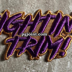 May include: Purple and gold embroidered patch with the text "Fighting Trim!" and the website "pgjoint.com".