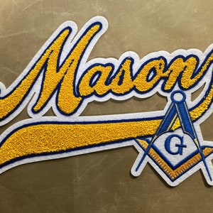 May include: A white felt patch with the word "Mason" in yellow cursive lettering. A blue and gold Masonic symbol is below the word.