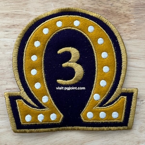 May include: A navy blue and gold patch with a horseshoe design and the number 3 in the center. The patch has a gold border and white dots around the horseshoe. The text "visit pgjoint.com" is at the bottom.