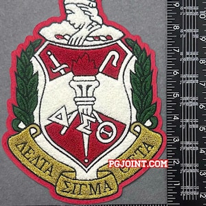 May include: A red, white, and green embroidered patch featuring a shield design with Greek letters and a torch. The patch has a gold banner with Greek text and the website PGJOINT.COM.