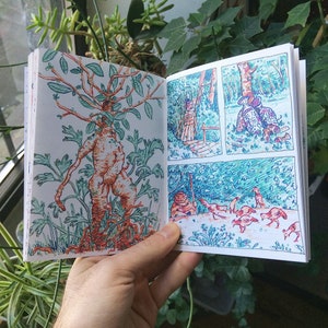 May include: Open comic book pages with colorful illustrations. One page features a humanoid plant with roots and leaves. The other page shows a forest scene with figures and animals, all drawn with blue, green, and orange ink.