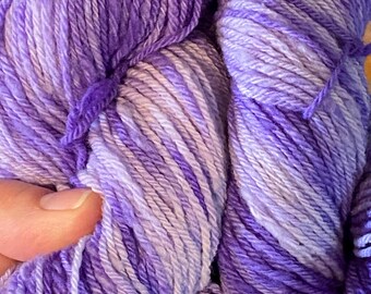 Könnte beinhalten: Nahaufnahme eines Knäuels violetter Wolle mit verschiedenen Lavendel- und Violetttönen. Das Garn ist eng gewickelt und zeigt die Textur der Fasern. Das Garn eignet sich für Strick- oder Häkelprojekte.