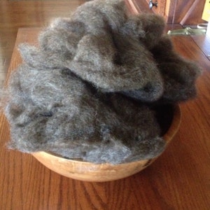 May include: A wooden bowl filled with a large amount of dark gray wool fibers.
