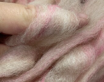 Könnte beinhalten: Nahaufnahme einer Handvoll weicher, flauschiger Fasern. Die Faser ist eine Mischung aus Weiß und blassem Rosa, mit Streifen von hellerem Rosa. Die Textur wirkt zart und luftig, geeignet für Bastelprojekte.