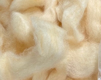 Könnte beinhalten: Nahaufnahme eines Haufens weicher, cremefarbener Wollfasern. Die Fasern sind flauschig und strukturiert, mit einem natürlichen, organischen Aussehen. Die Wolle scheint unverarbeitet und bereit für die Verarbeitung zu sein.