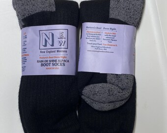 Könnte beinhalten: Zwei Paar schwarze und graue Alpaka-Stiefelsocken. Jedes Paar ist mit einem lila Etikett versehen, auf dem "New England Woolens" und "Rain or Shine Alpaca Boot Socks" steht. Die Socken werden in den USA hergestellt.