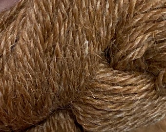 Könnte beinhalten: Nahaufnahme eines eng gewickelten, dicken braunen Garns. Das Garn hat ein strukturiertes Aussehen mit sichtbaren Fasern und einer leicht unebenen Oberfläche. Die Farbe ist ein warmes, erdiges Braun, was auf eine Naturfaser wie Wolle oder Baumwolle hindeutet.