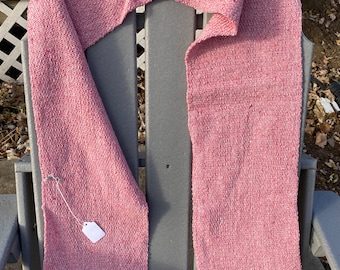 Könnte beinhalten: Ein rosa gewebter Schal mit einem strukturierten Muster. Der Schal ist in der Mitte gefaltet und über einen grauen Stuhl gelegt.