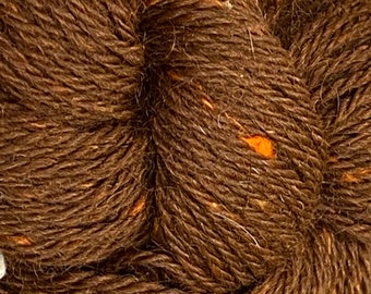Könnte beinhalten: Nahaufnahme eines Strangs braunen Garns mit orangefarbenen und weißen Flecken. Das Garn ist eng gewickelt und zeigt die Textur der Fasern. Dieses Garn eignet sich zum Stricken, Häkeln und für andere Textilkunstprojekte.