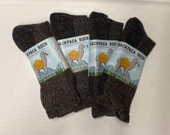 Könnte beinhalten: Vier Paar braune Backpaca-Socken, leichte Sport-Wandersocken. Jedes Paar hat ein Etikett mit einem Kamel, das einen Rucksack trägt. Die Socken werden in den USA mit in den USA angebauter Alpaka hergestellt.