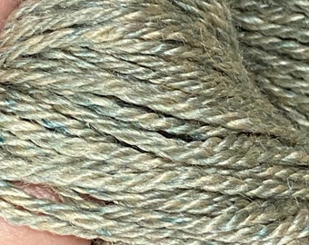 Könnte beinhalten: Nahaufnahme eines Garnknäuels in Grün-, Beige- und Blautönen. Das Garn ist fest verdreht und zeigt die Textur und die einzelnen Stränge. Die Farbvariation verleiht dem Garn ein gesprenkeltes Aussehen, geeignet für Strick- oder Häkelprojekte.