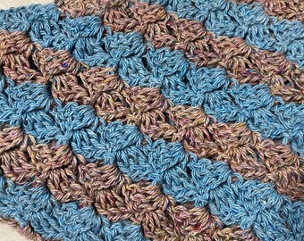 Könnte beinhalten: Nahaufnahme eines gehäkelten Textils mit einem strukturierten, erhabenen Muster. Das Garn ist eine Mischung aus blauen, braunen und rosa Farbtönen, die eine visuell interessante und taktile Oberfläche erzeugt. Die Häkelarbeit wirkt dicht und gut verarbeitet.
