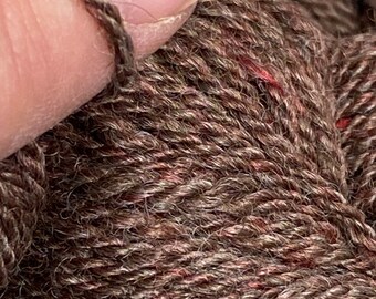 Könnte beinhalten: Nahaufnahme von braunem Garn mit strukturierter Optik. Das Garn hat eine Mischung aus braunen und rotbraunen Fasern, wodurch ein melierter Effekt entsteht. Das Bild zeigt die Textur und die Details des Garns, geeignet für Strick- oder Häkelprojekte.
