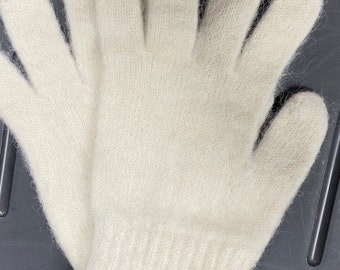 Könnte beinhalten: Ein Paar elfenbeinfarbene Handschuhe. Diese gestrickten Handschuhe sind aus einem weichen, flauschigen Material gefertigt. Die Handschuhe sind so konzipiert, dass sie die gesamte Hand bedecken, einschließlich der Finger und des Handgelenks. Die Handschuhe sind wahrscheinlich für kaltes Wetter.