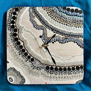 May include: A square clock with a white background and a black clock face. The clock face is decorated with a pattern of black, gray, and white dots that resemble an agate stone. The clock hands are black.