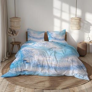 May include: A bed dressed with a blue and white abstract watercolour-style duvet cover and two matching pillowcases. The bedding is on a wooden bed frame, and the room has a neutral colour palette with woven pendant lights and a round jute rug.