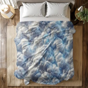 Può includere: Un copriletto bianco e blu con un design testurizzato a forma di nuvola. Il copriletto è piegato al centro e si trova su una superficie di legno.