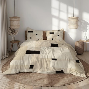 May include: A cream-colored bed set with a geometric design of black and beige rectangles and squares. The set includes a duvet cover and two pillowcases. The bed is made up with a wooden headboard and is set on a round, woven rug.