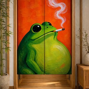 Peut inclure: Un rideau de porte rectangulaire en tissu présentant un fond orange vif avec une grande grenouille verte au corps rond au premier plan. La grenouille a de grands yeux noirs et tient une cigarette allumée dans sa bouche, avec de la fumée blanche.