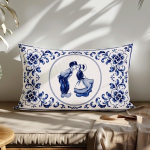 Könnte beinhalten: Ein rechteckiges Dekokissen mit weißem Grund und blauem Blumenmuster am Rand. In der Mitte befindet sich eine kreisförmige Illustration von zwei Personen in traditioneller Kleidung, die sich küssen, im klassischen blau-weißen Porzellanstil.