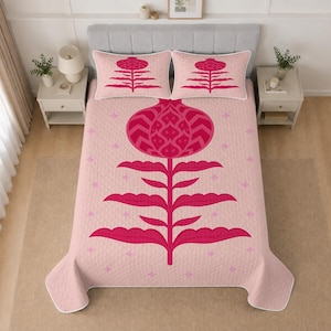 Pode incluir: Uma colcha acolchoada rosa-claro e duas fronhas a condizer com um grande motivo floral ou de romã estilizado em rosa-escuro centrado em cada peça. O design inclui folhas simétricas e pequenos detalhes em forma de estrela no tecido.