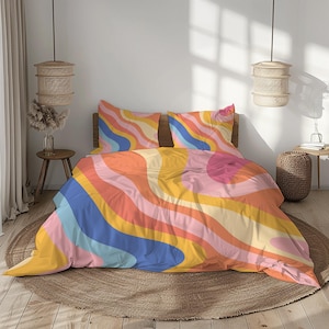 Peut inclure: Un lit avec une parure de lit abstraite et colorée. Le motif présente des rayures ondulées dans les tons de rose, orange, jaune, bleu et pêche. Deux taies d'oreiller assorties sont visibles. Le lit est posé sur un tapis rond tissé.