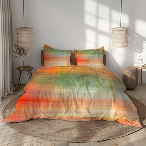 Op de afbeelding: Een kleurrijk beddengoed met een abstract ontwerp. De set bevat een dekbedovertrek en twee kussenslopen, met oranje, groene en gele tinten. Het beddengoed ligt op een bed met een houten hoofdbord, wat een warme sfeer creëert.
