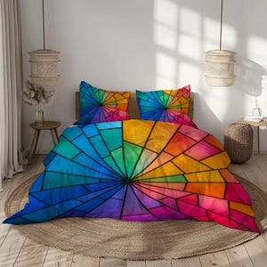 May include: A colourful bedding set with a stained-glass design. The set includes a duvet cover and two pillowcases, featuring a radial pattern in shades of blue, green, yellow, orange, and pink. The design is framed by black lines.