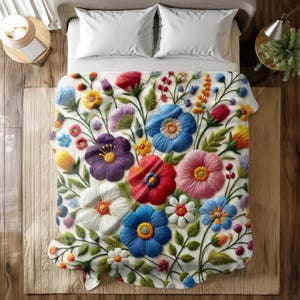 Puede incluir: Una manta blanca bordada con un diseño floral. La manta presenta una variedad de flores coloridas, incluyendo azules, rojas, moradas y amarillas. Las flores tienen costuras detalladas y están dispuestas en un patrón vibrante. La manta está sobre una cama con almohadas blancas.