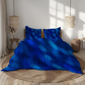 May include: A blue bedding set with a watercolor-style design. The set includes a duvet cover and two pillowcases. The color palette features shades of blue, creating a calming and artistic aesthetic. The bed is on a round, woven rug.